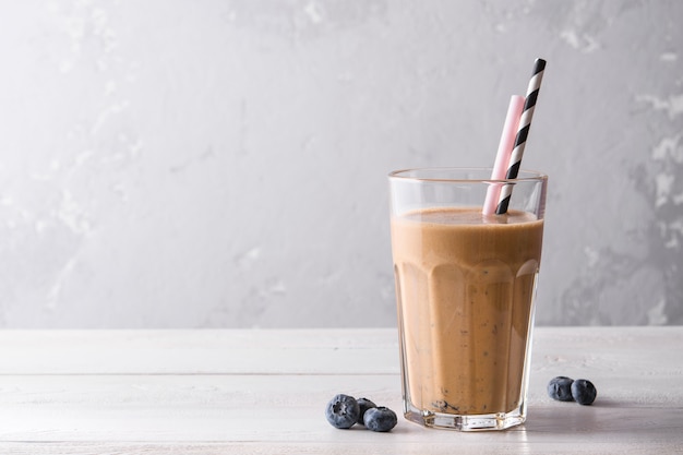 Batido de proteína de chocolate sobre un fondo blanco de madera. Batido fresco con arándanos en una mesa de luz. Un vaso de batido de chocolate.