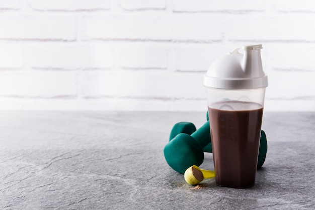 Batido de proteínas de chocolate y pesas sobre piedra gris