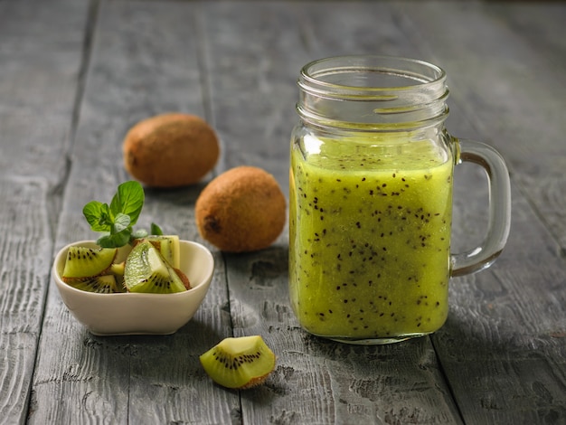 Batido recién preparado de rodajas de kiwi, manzana, menta y kiwi sobre la mesa rústica negra