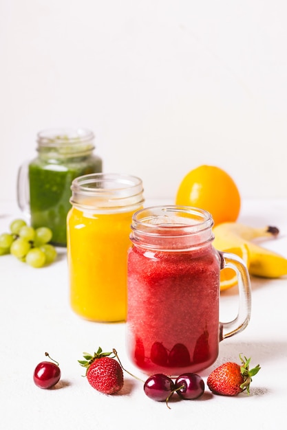 Batido rojo, amarillo y verde en un frasco de vidrio e ingredientes.