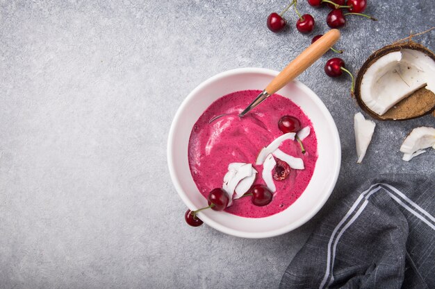 Batido rosa de plátano y cereza Granola y trozos de coco en la parte superior. Desayuno saludable de verano, vista superior