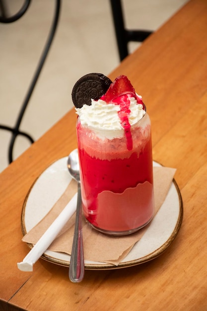 batido de terciopelo rojo con cobertura de crema batida de fresa y frutos rojos y jarabe de fresa sobre una mesa de madera