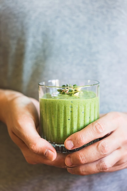 Batido vegano verde con espinacas, plátano y semillas germinadas en vaso en manos masculinas