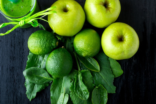 Batido verde cerca de ingredientes para él sobre fondo de madera negra. Manzana, lima, espinacas. Desintoxicación Bebida saludable.