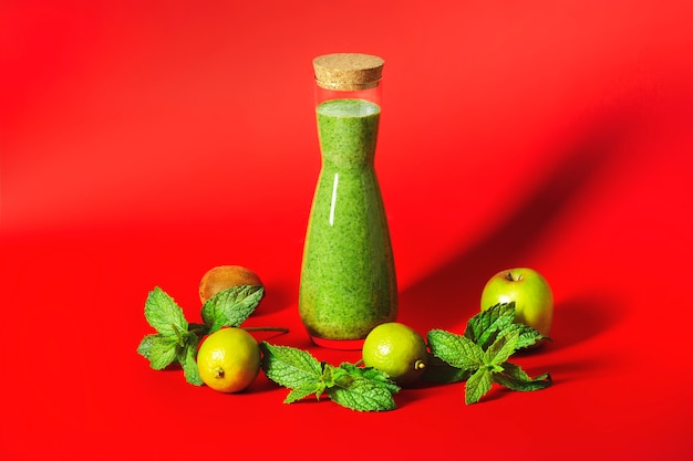 Batido verde en una hermosa botella alta sobre un fondo rojo.