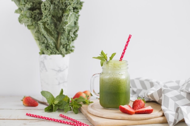 Batido verde con kale menta y fresa servido en un tarro con paja roja