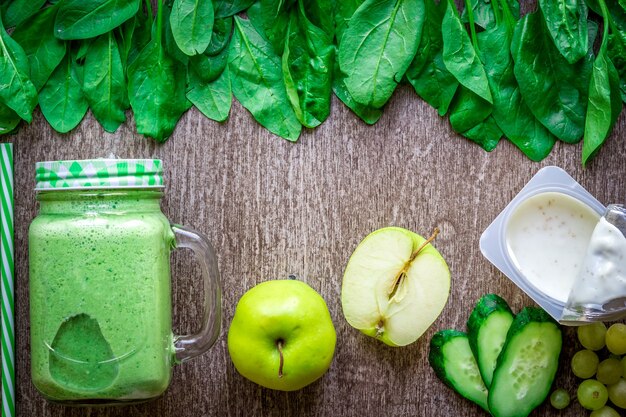 Batido verde con manzanas, yogur, espinacas, pepino sobre fondo de madera