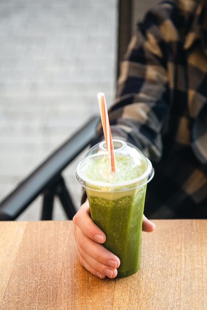 Batido verde en una mesa en el café Hombre sano bebiendo batido de proteína de dieta de desintoxicación Mano sosteniendo un vaso de plástico de jugo de vegetales alimentos saludables comer estilo de vida