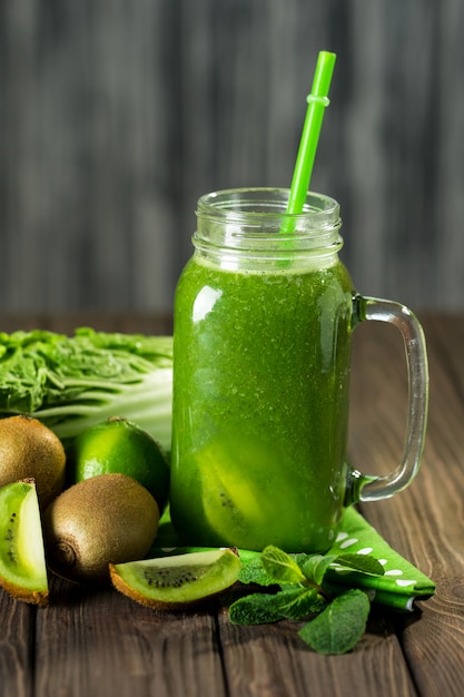 Batido verde mezclado con ingredientes en la mesa de madera