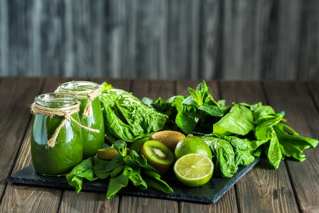 Batido verde mezclado con ingredientes en el tablero de piedra, madera