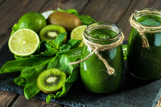 Batido verde mezclado con ingredientes en el tablero de piedra, mesa de madera