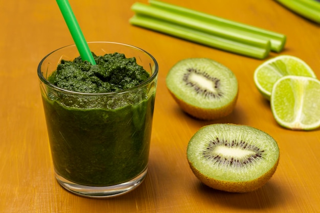 Batido verde y paja en vaso Kiwi y rodajas de limón tallos de apio en la mesa