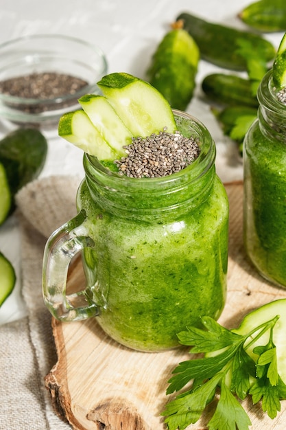 Batido verde con pepino en un frasco de vidrio. Verduras frescas maduras, verduras y semillas de chía. Luz dura de moda, sombra oscura. Fondo de masilla blanca, cerrar