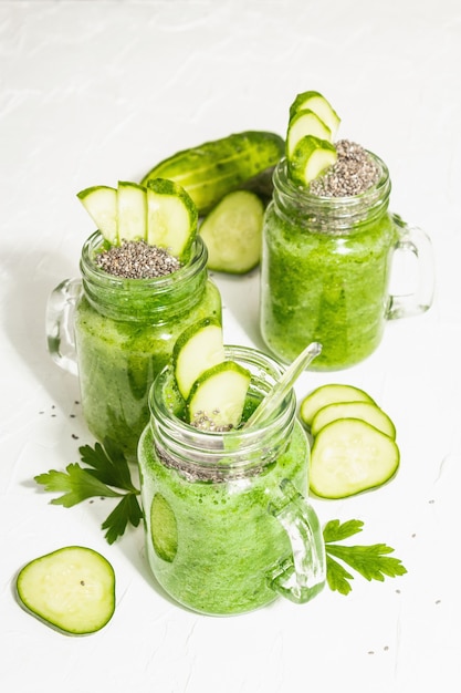 Batido verde con pepino en un frasco de vidrio. Verduras frescas maduras, verduras y semillas de chía. Luz dura de moda, sombra oscura. Fondo de masilla blanca, cerrar