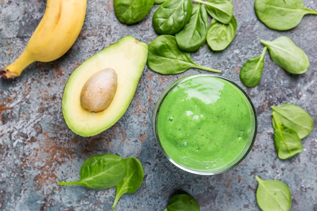 Batido verde saludable con espinacas, aguacate, plátano y semillas de chía en frascos de vidrio sobre fondo de piedra gris, vista superior.