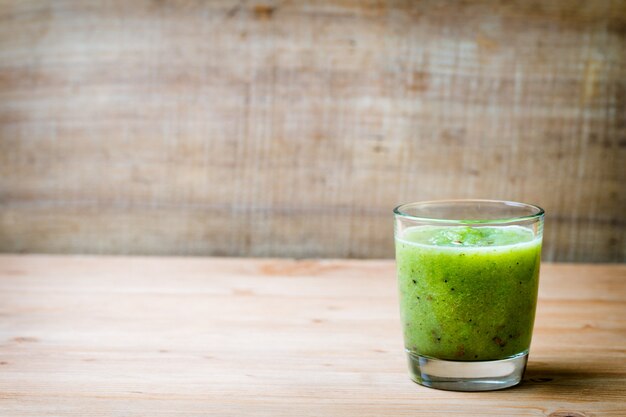 Batido verde saludable en un vaso sobre madera vieja.