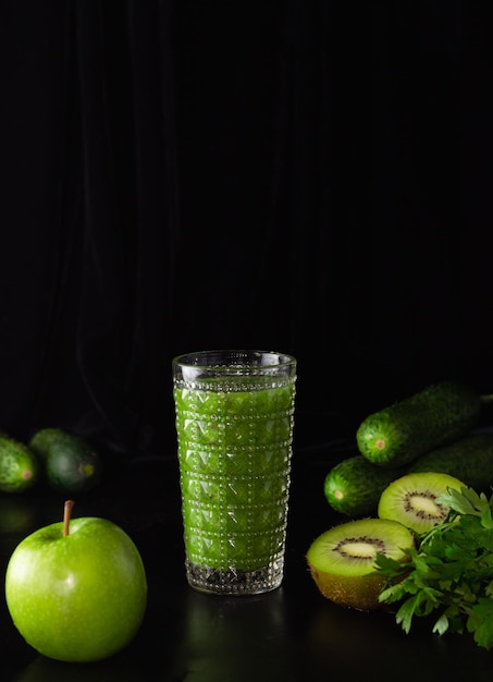 Batido verde en un vaso de vidrio sobre un fondo negro. Kiwi, manzanas, pepinos y verduras. Cocinar comida sana.