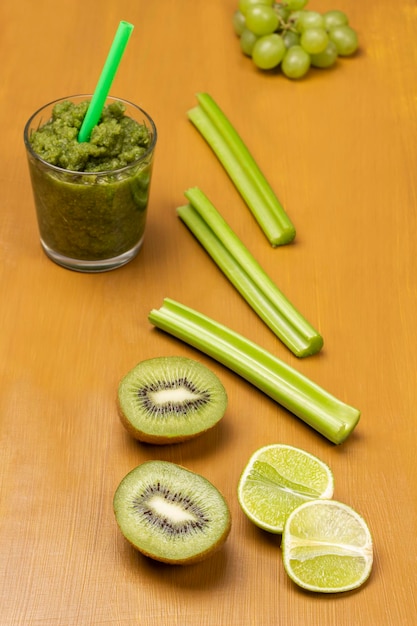 Batido verde en vidrio Limón y kiwi mitades tallos de apio y uvas en la mesa