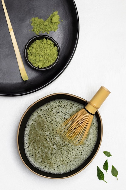 Batidor de bambú en un recipiente con té matcha Cuchara dosificadora y polvo de té matcha en un plato negro