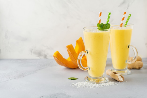 Batidos de calabaza con jengibre y virutas de coco y menta en un vaso sobre piedra clara o superficie de hormigón. Bebida saludable y deliciosa para el desayuno. Enfoque selectivo. Vista superior.