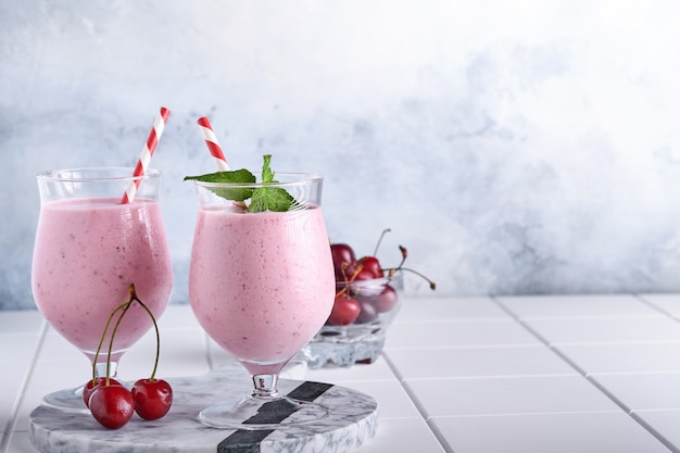 Batidos de cereza rosa con frutos rojos frescos, semillas de chía, hojas de color verde menta, fondo de cocina de piedra blanca. Enfoque selectivo.