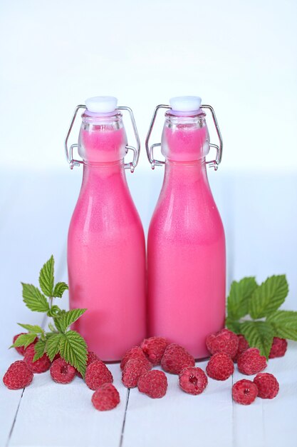 Batidos de color rosa en una botella de vidrio con frambuesas, manzanas en madera azul