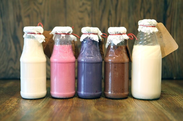 Batidos de colores en botellas Batido de leche de bebida colorida en botella con verduras frescas en madera