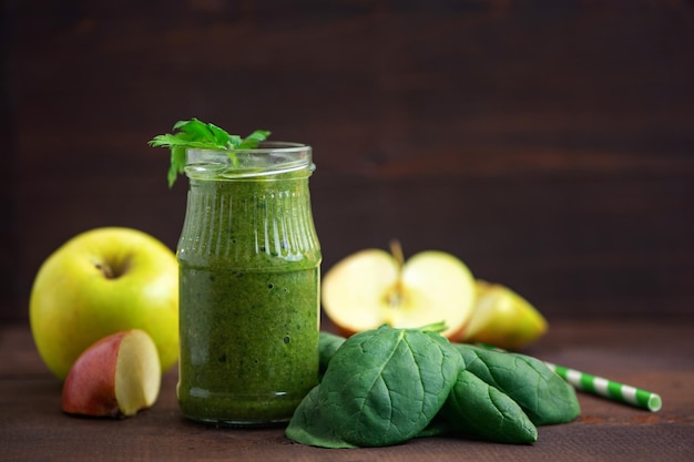 Batidos de espinacas verdes en vidrio con ingredientes en la mesa de madera oscura Vista lateral