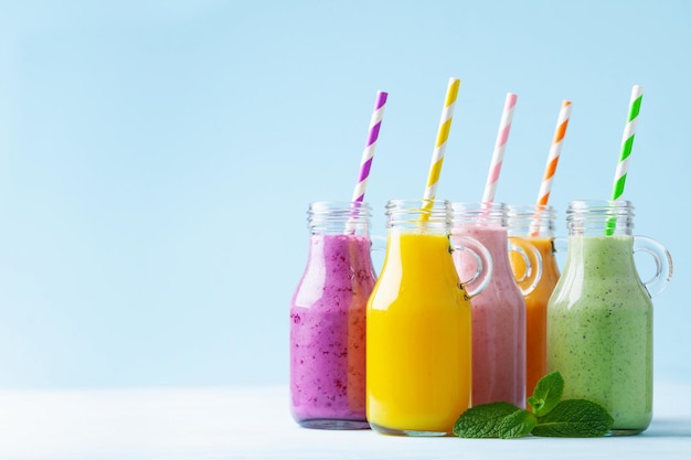 Batidos de frutas coloridos de verano en frascos sobre fondo azul Concepto de comida dietética y desintoxicación saludable