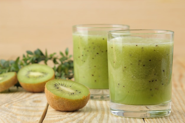 Batidos de kiwi en un vaso junto a rodajas de kiwi fresco sobre una mesa de madera natural.