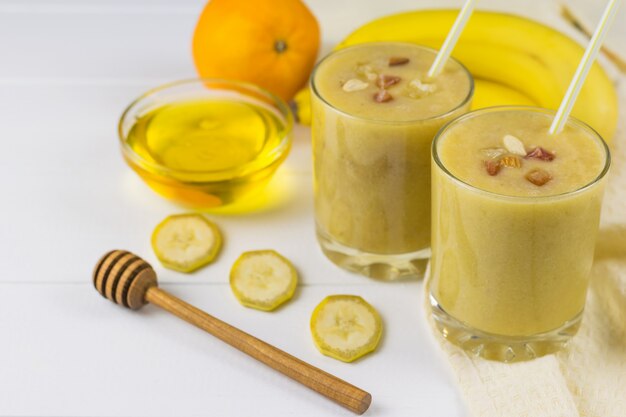 Batidos recién hechos con mango, plátano, naranja, miel, nueces y cereales en una mesa de madera blanca