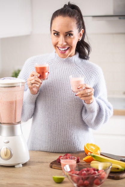 Batidos veganos de frutas y yogur vegetariano en taza sostenida por una mujer guapa en casa.