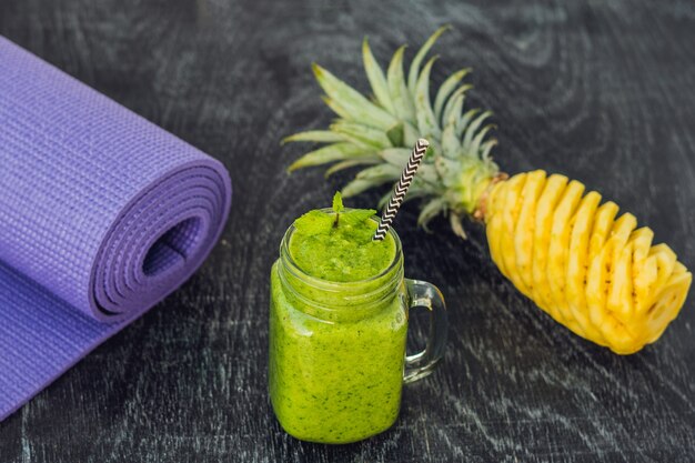 Batidos verdes de espinaca y piña y esterilla de yoga. Concepto de alimentación y deportes saludables.