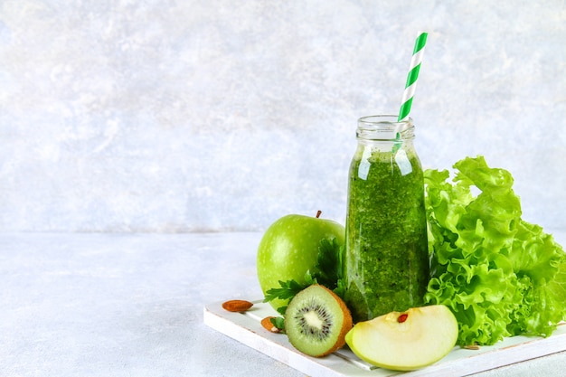 Batidos verdes de perejil, ensalada, kiwi, manzana en una botella en una mesa de concreto gris.