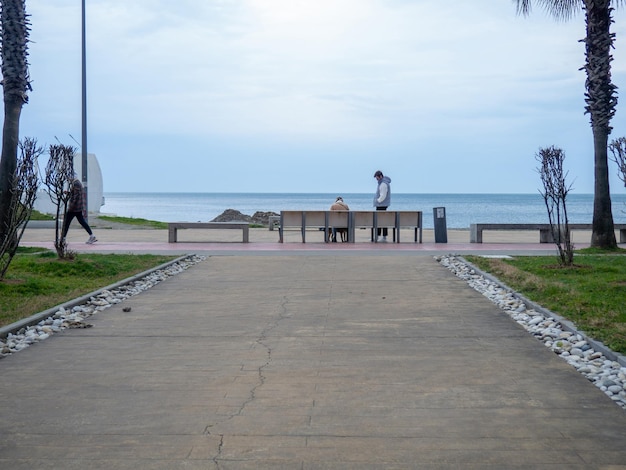 Batumi Geórgia 01282023 Estrada no parque que leva ao mar Costa do Mar Negro Parque na Geórgia Zona pedonal Lindo lugar Nublado Pessoas no banco