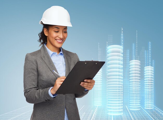 Bau-, Entwicklungs-, Konstruktions- und Architekturkonzept - lächelnde Geschäftsfrau im weißen Helm mit Zwischenablage