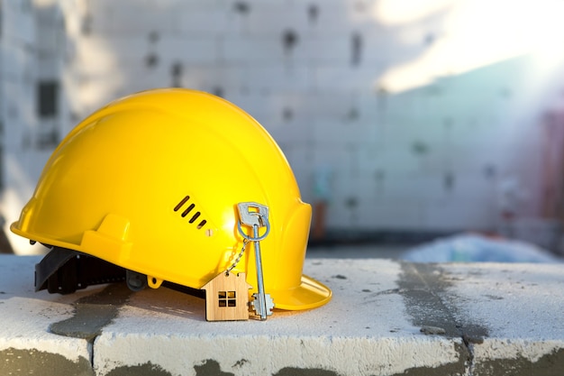 Bau gelber Bauarbeiterhelm und Schlüssel zum Haus am Fenster des Gehäuses aus Blöcken aus porösem Beton. Schlüsselfertiges Bauen, zukünftiges Zuhause, Ingenieurwesen, Bauen. Arbeitssicherheit. Platz kopieren