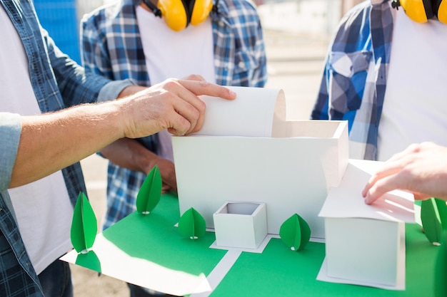 Bau-, Konstruktions-, Teamarbeits- und Personenkonzept - Nahaufnahme der Hände des Bauherrn mit Papierhausmodell oder Layout im Freien