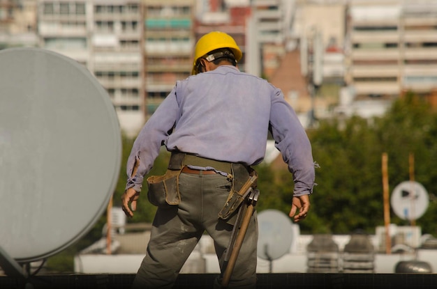 Bauarbeiter Arbeiter auf der Terrasse eines Gebäudes mit Arbeitskleidung und gelbem Helm und mit einem Gürtel mit Werkzeugen