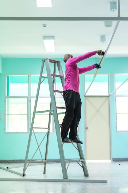 Bauarbeiter, der auf Aluminiumtreppe oder Leiter unter Verwendung eines messenden Bands steht.