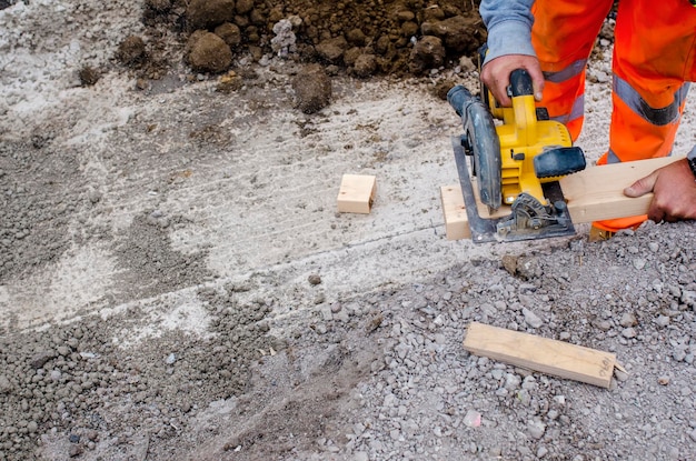 Bauarbeiter, der auf der Baustelle Holz mit einer schnurlosen, batteriebetriebenen Kreissäge schneidet