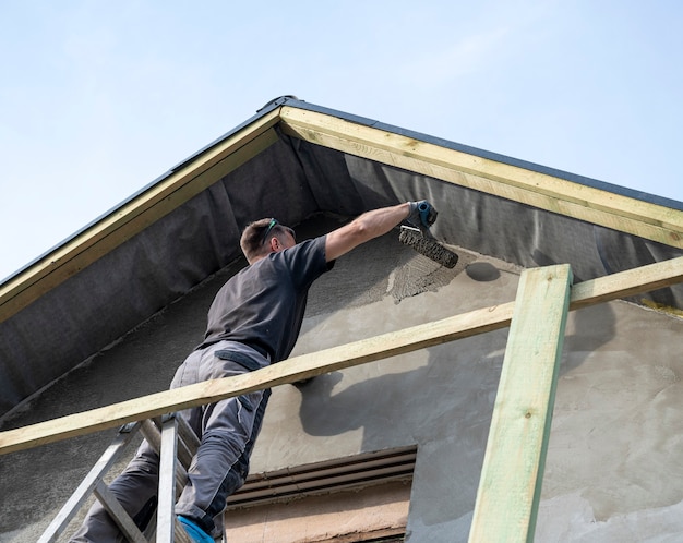 Bauarbeiter, der die fassade des hauses verputzt. auftragen von fassadenputz