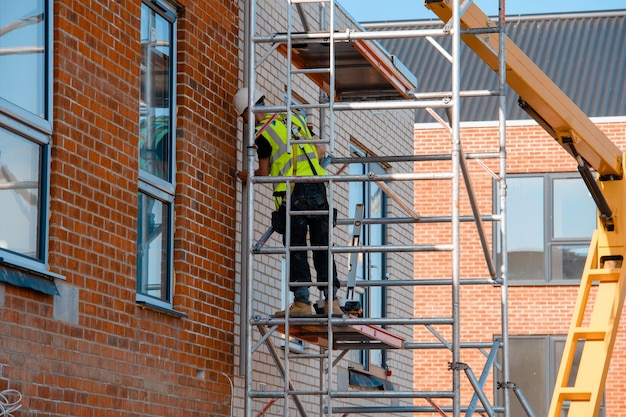 Bauarbeiter, die einen mobilen Aluminiumgerüstturm und einen Sicherheitsgurt verwenden, um in der Höhe zu arbeiten