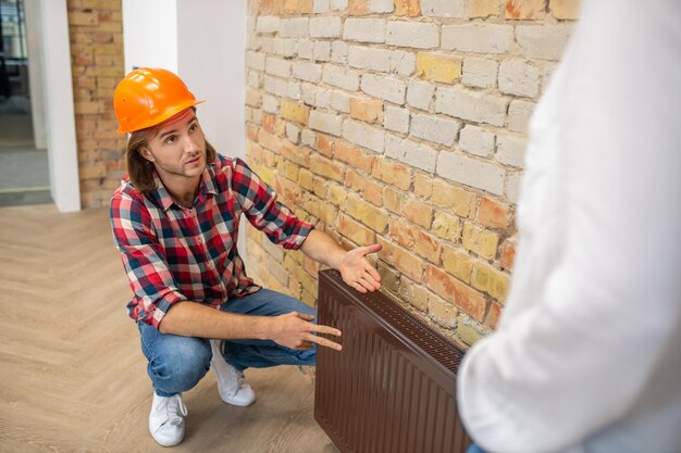 Bauarbeiter im orangefarbenen Helm, der einem Kunden etwas erklärt