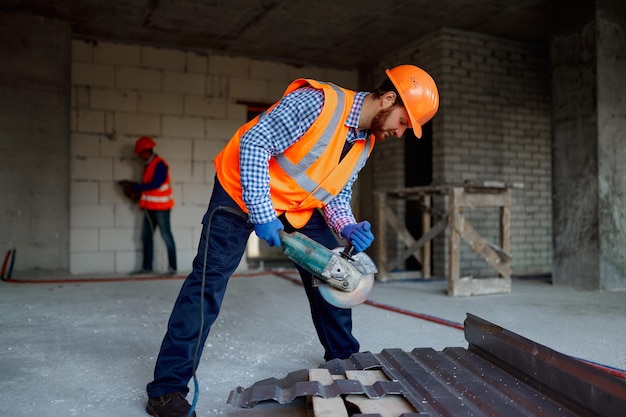 Bauarbeiter in Uniform mit Schleifmaschine zum Schneiden von Metallteilen auf der Baustelle