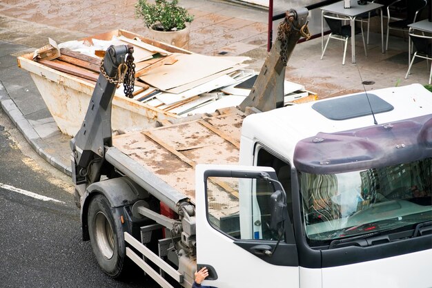 Foto bauarbeiter mit einem metallbehälter in einem lastwagen mit trümmern und holzabfällen