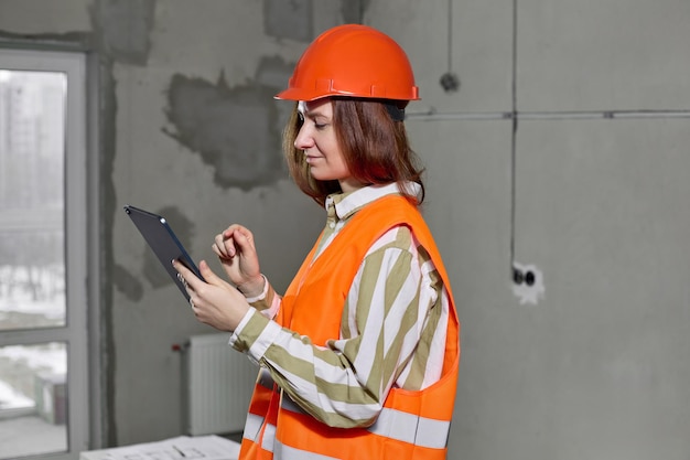 Bauarbeiterin mit Schutzhelm und Weste benutzt ein Tablet zum Entwerfen