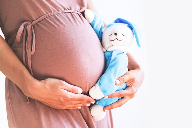 Bauch der schwangeren Frau der Nahaufnahme mit Teddybär-Schwangerschaftskonzept