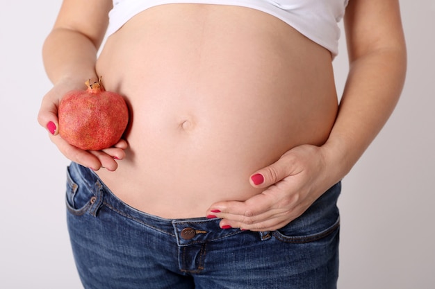 Bauch der schwangeren Frau mit Granatfrucht, gesundem Essen und Schwangerschaft