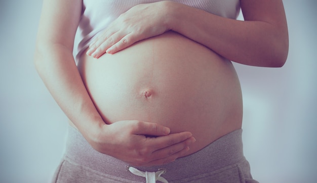 Bauch einer schwangeren Frau auf hellem Hintergrund